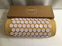 Front view of the Shakti pillow with 7 rows of circular white spiked discs on a yellow fabric base and the brown Shakti branded box behind it.