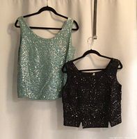 Two vintage sleeveless tops hanging on black hangers against a white background, showing full front views.
