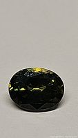 Close-up image of an oval cut multicolored sapphire showing green base color with yellow and orange internal reflections.