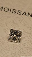 Close-up image showing the top facet and the clarity of the princess cut moissanite gemstone on GRA certificate paper.