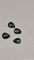 Four pear cut natural sapphires in blue and green hues shown against a plain background.