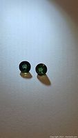 Pair of round cut multicolored blue-green sapphire gemstones on white surface showing color and facets