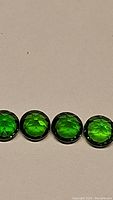 Close-up photo showing four round green faceted chrome diopside stones in a line on a neutral background.
