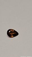 Pear-shaped cognac brown zircon gemstone shown from top view on white background, highlighting brilliant facets and clean clarity.