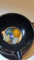 Five polished oval cabochon Ethiopian opals in a black dish showing colors and flash typical of untreated stones from the Pita Ridge area.