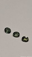 Three oval cut natural green apatite gemstones with deep green color and high clarity on a light background.