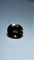 Top-down view on flat surface showing dark blue-green oval sapphire with reflective facets.