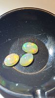 Image showing three oval cabochon opals with rainbow flashes inside a black container, displaying natural color play.