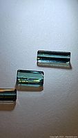 Photo showing three rectangular step-cut Paraiba blue-green tourmaline gemstones on a white background with clear detail and light reflection.