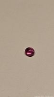 Bright pink oval cabochon sapphire on plain beige background showing natural inclusions and glossy surface