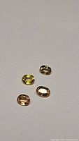 Four oval cut natural sapphires in yellow and orange hues shown on neutral background.