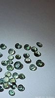 Group of small round faceted green gemstones on a white background under neutral light