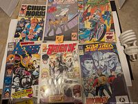 Photo showing all six comic books laid out flat on a carpet. Titles include Chuck Norris Karate Kommandos, two Star Trek The Next Generation issues, Spider-Man, Avengers, and Brigade.