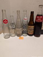Full view of six vintage soda bottles lined up side-by-side on white surface, showing all labels and bottle shapes