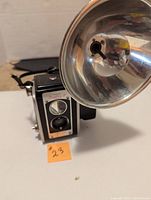 Front view of Kodak DWAflex III box camera showing lens, shutter dial and attached large metal reflector flash holder.