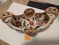 Top and interior view of an oval ceramic basket with floral and bird designs, showing its size and intricate painted details.