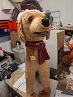 Front view of plush Christmas dog wearing red plaid scarf and Santa hat, shows facial details.
