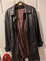 Front view of black leather jacket by Danier with brown patterned lining, hanging on a hanger.