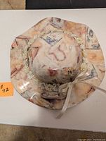 Top view of the white glass hat showing round crown with floral, rose and vintage postcard motif, flower garland and ribbon tie.