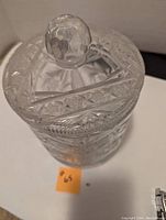 Front and top view of clear crystal ice bucket with cross-hatched and starburst cut designs, lid with large faceted spherical handle.