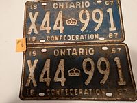 Front side of two matching 1967 Ontario license plates with blue background and white embossed alphanumeric characters and confederation markings.