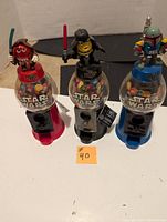 Front view of three M&M Star Wars coin dispensers in red, black, and blue with corresponding M&M character toppers and filled with candy.