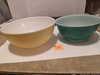 Two Pyrex mixing bowls side by side showing green and yellow colors with white interiors.