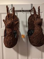 Two woven deer head planters hanging on the back of a door, showing overall size and shape.