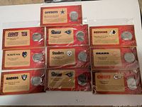 Photo showing 10 Budweiser Superbowl collector coins, each with individual card describing specific NFL Superbowl champions from various teams, sealed in plastic.