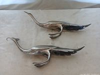 Pair of silver plated bird figurines placed horizontally, showing elongated wings and curved necks
