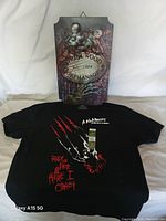 Photo showing metal Springwood Orphanage sign with spooky baby dolls and skeletal hand, alongside black Nightmare on Elm Street t-shirt with claw graphic and text.