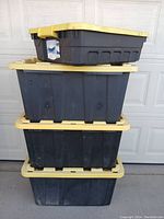 Four black plastic storage tubs stacked with yellow lids, showing size variation and general condition.