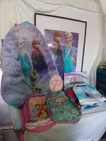 Lot overview showing pop-up hamper, framed Frozen wall art, backpacks, and bedding.