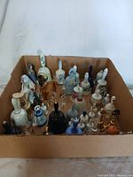 Top angled view of the cardboard box holding over 30 assorted ceramic bells showing variety in color, size, and design.