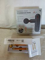 Box and contents of Sharper Image Powerboost Move Percussion Massager with user manual and packaging label.
