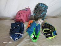 Five colorful kids baseball gloves arranged with a baseball on a beige surface