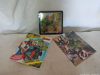 Photo of Crayola tin box, Avengers coloring booklet, and poster showing fronts and overall condition of items.