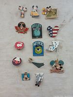 Photo of 14 assorted Disney pins laid flat on fabric background including Mickey Mouse, Sulley, Mike Wazowski, Olaf, and others.