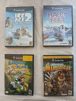 Four Nintendo GameCube games arranged on a white surface, showing front covers for Ice Age 2 The Meltdown, Happy Feet, Looney Tunes Acme Arsenal, and Madagascar.