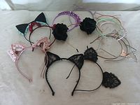 Lot of 15 assorted kids cat ear headbands photographed all together on white surface showing variety of colors and styles including lace, fabric, floral, plastic, and metal designs.