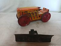 Orange and yellow metal toy tractor with red wheels, missing one tread strip placed in front.