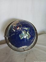 Front view of the mineral stone world globe showing Asia and Australia with semi-precious stone overlays and metal meridian ring.