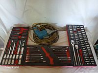 Photo showing socket set organized in black and red foam with various ratchets, sockets, extensions, and tools, alongside the electric drill coiled with extension cord.