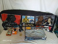 Overview of the lot with Star Wars pillowcase, X-Wing Fighter model kit, bobbleheads and coins spread on black cloth.