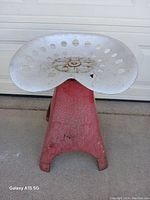 Front angled view of the metal yard art seat showing the white perforated seat and red base with wear.