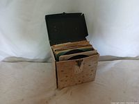 A badly worn and damaged vintage record case open and filled with 45 RPM records upright inside.