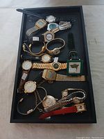 Photo showing assorted watches in black tray including digital and analog types with various band materials and colors
