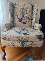 Front view of Queen Anne style wingback armchair showing floral upholstery and wooden cabriole legs.