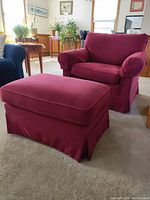 Red fabric armchair and ottoman set in living room setting, angled view