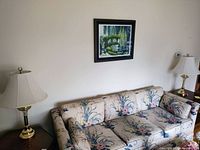 Photo showing the matching pair of brass table lamps on wooden side tables beside floral sofa.